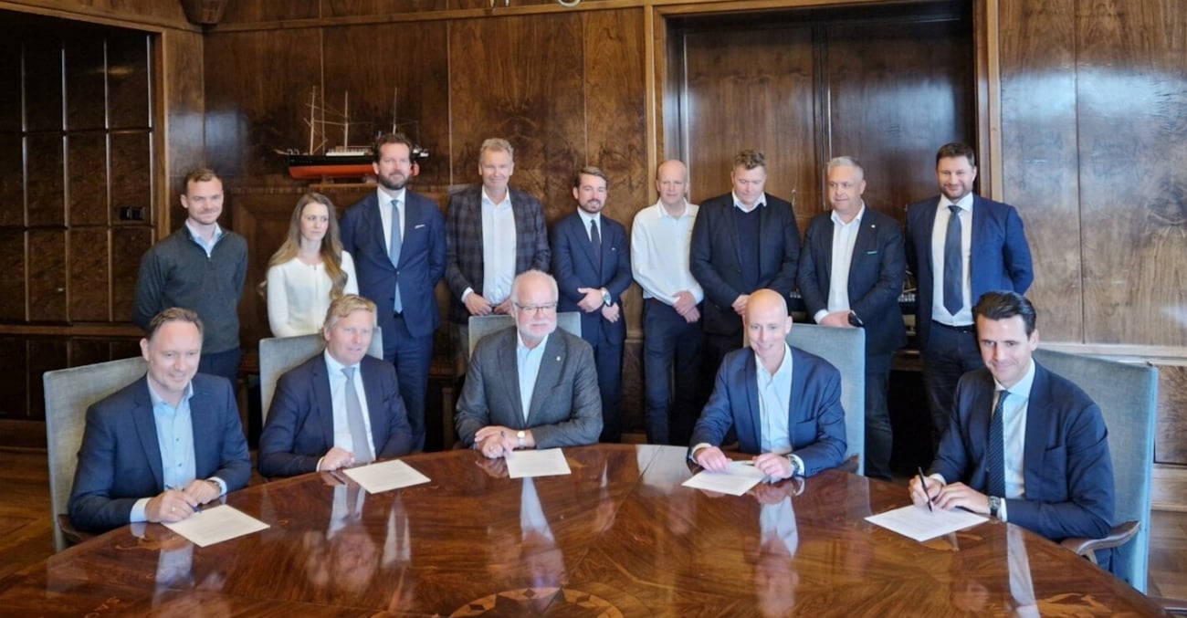 Blide mennesker som sitter ved et bord og signerer et dokument.