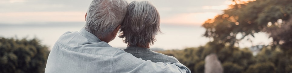 To eldre personer på en benk som ser utover havet