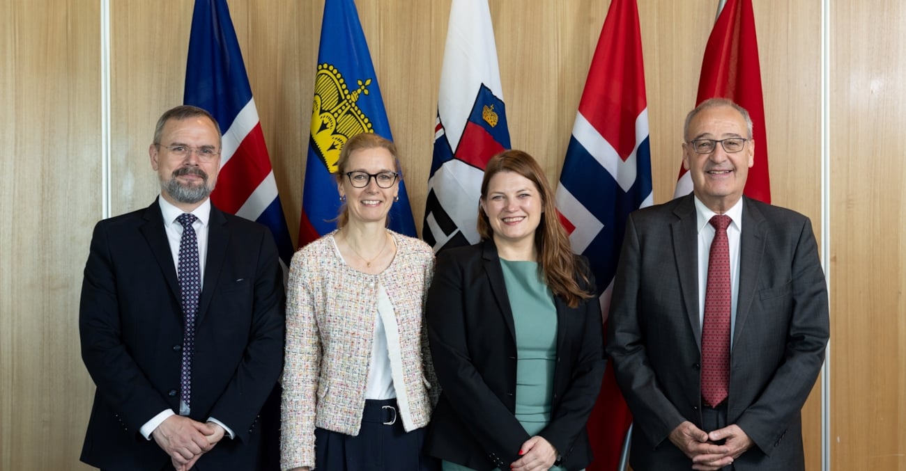Fire smilende mennesker foran flaggene til EFTA-landene
