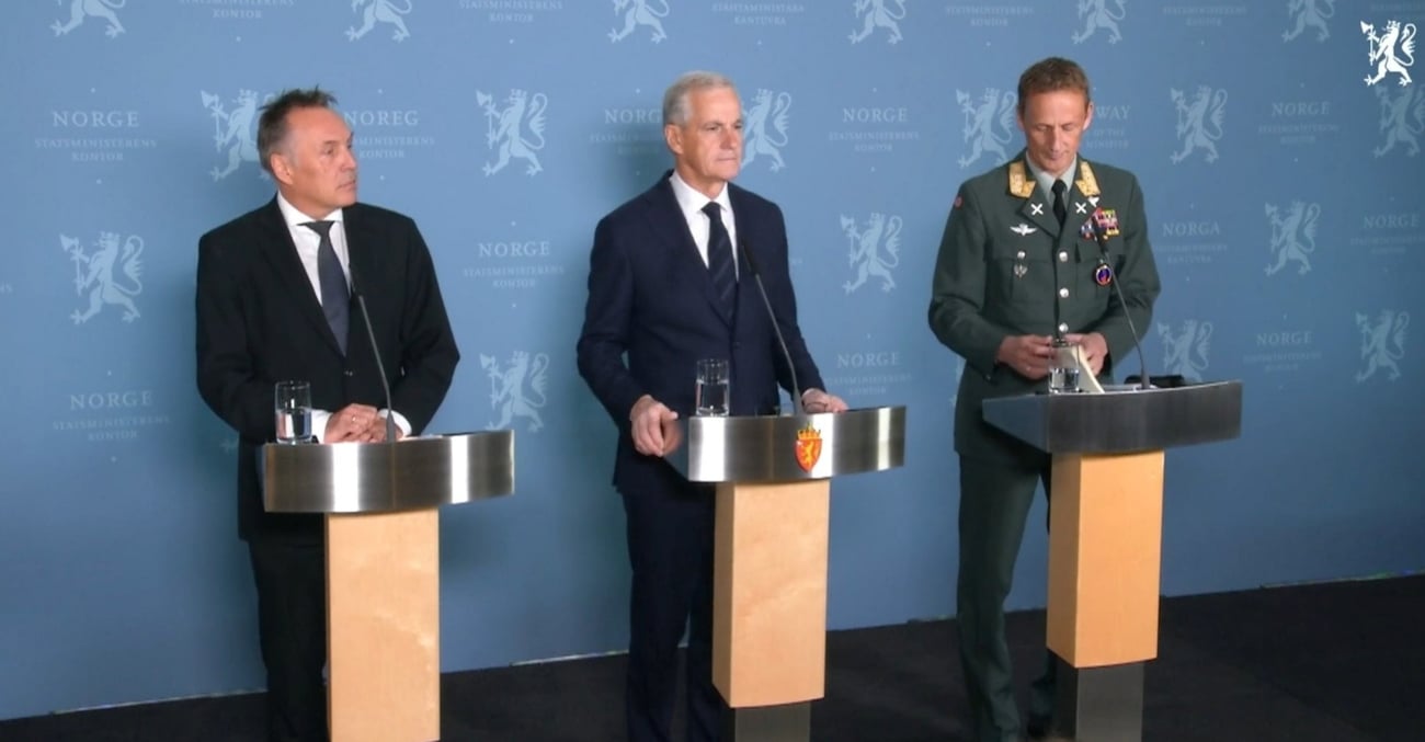 Tre menn på en scene bak talerstoler