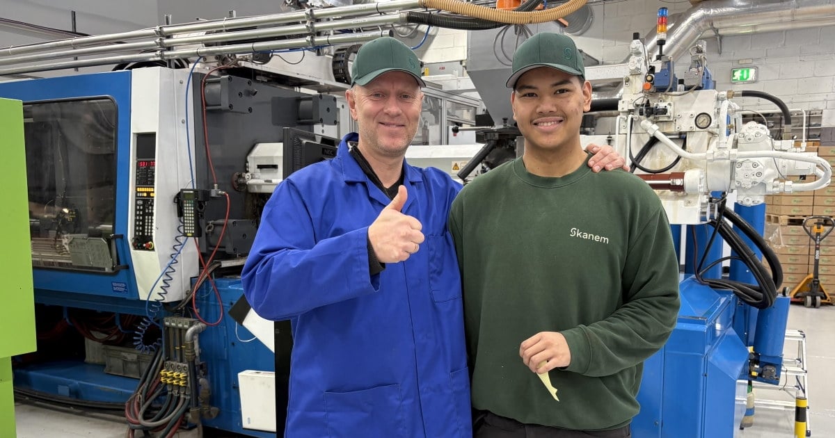 To mennesker som smiler og er kledd i arbeidsuniform inne i et produksjonslokale