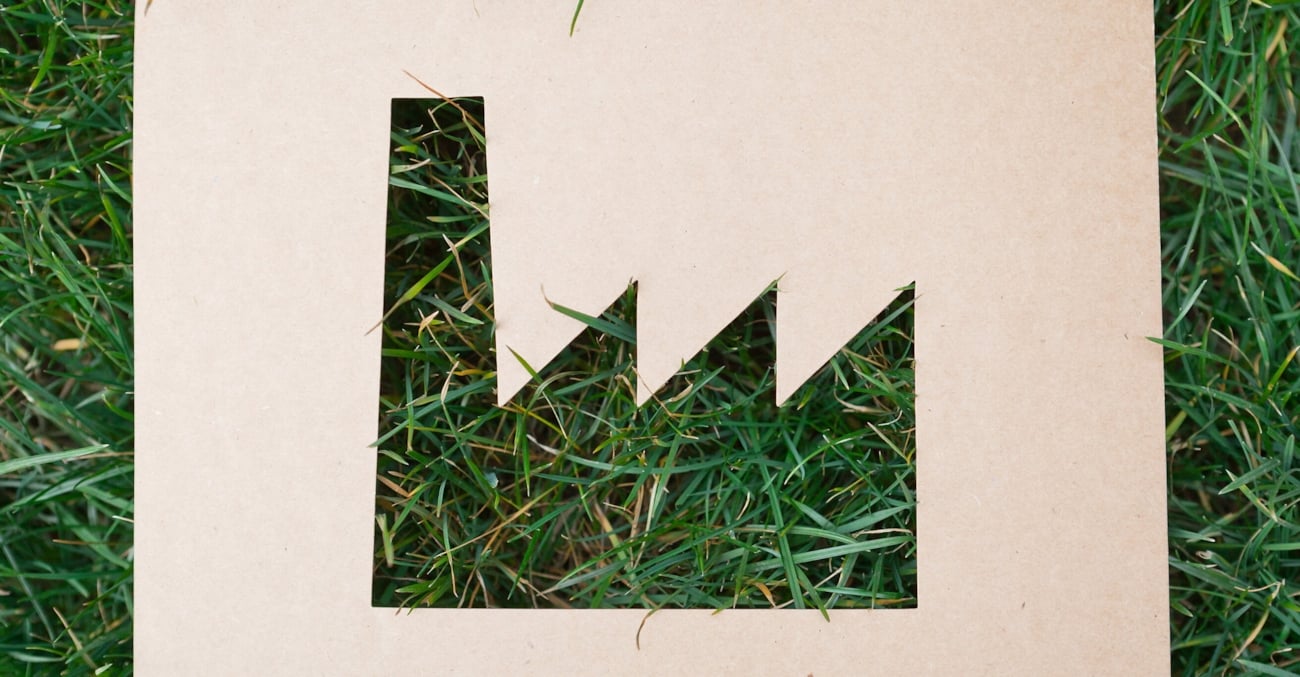 Illustrasjon - fabrikk-symbol klippet ut i papp som ligger på gress